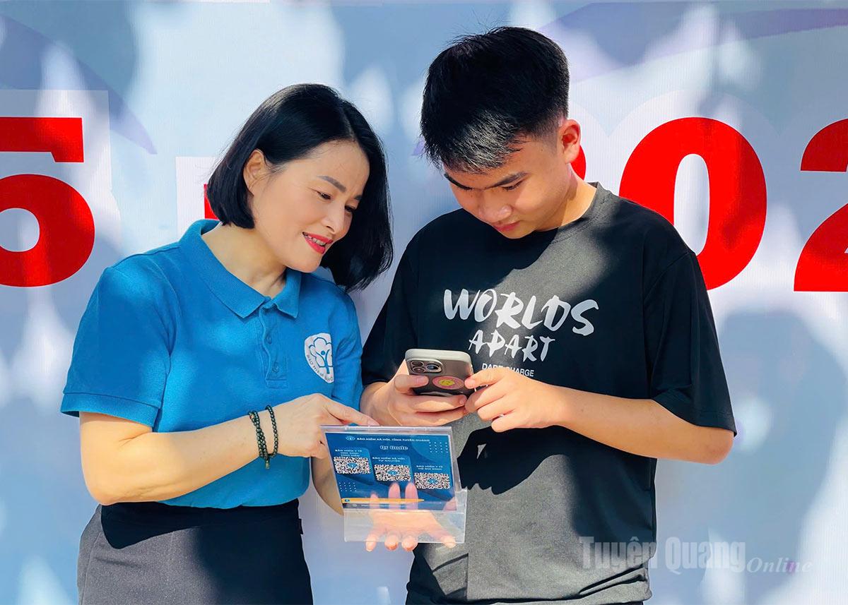 Cán bộ BHXH tỉnh hướng dẫn sinh viên quét mã QR đọc thông tin về chính sách BHYT học sinh, sinh viên